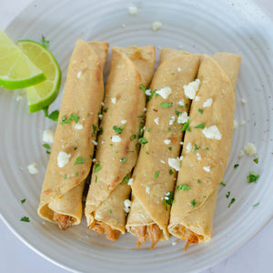 Nature's Choice plant-based, vegan taquitos on a white plate topped with cotija cheese and cilantro with two lime wedges on the side.